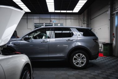 Gümüş rengi bir Range Rover Discovery, iyi aydınlatılmış bir garajda, döşemesiz, parlak ışıklandırmalı, ve yakınlarda bakım yapılan beyaz bir araba var..