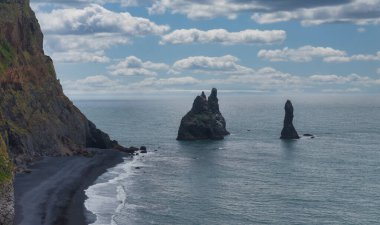 Reynisdrangar deniz yığınları İzlanda 'daki Reynisfjara Kara Kum Sahili yakınlarında okyanustan yükseliyor. Volkanik kum, kayalıklar ve bulutlar dramatik bir sahne yaratır..