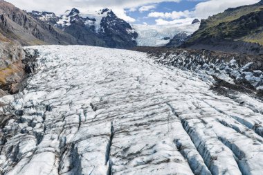 İzlanda 'da engebeli tepelere doğru uzanan derin yarıkları olan bir buzul. Dik kayalıklar ve yosun kaplı yamaçlar bulutlu bir gökyüzünün altındaki buzlu engin alanı sarar..
