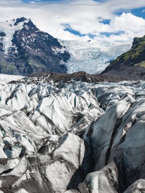 Sivri uçlu, buzla kaplı bir buzulun ön planda hakimiyeti vardır. Kar ve yeşil bitkilerle kaplı engebeli bir dağ sırasına kurulmuştur..