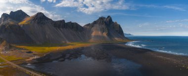 İzlanda 'daki Stoksnes Yarımadası' nda sivri uçlu Vestrahorn dağı, siyah kum plajı, yumuşak okyanus dalgaları ve yumuşak doğal ışık bulunur..