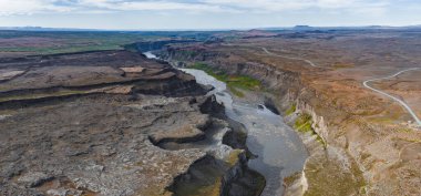 İzlanda 'daki Studlagil Kanyonu' nun havadan görünüşü, bazalt sütunlar, kıvrımlı bir nehir, dik kayalıklar ve engebeli araziye paralel uzanan bir yol..