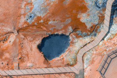 İzlanda 'da canlı turuncu ve kırmızı toprak tonlarıyla jeotermal alan, karanlık köpüren bir çamur havuzu, ve manzarayı saran tahta kaldırımlar..