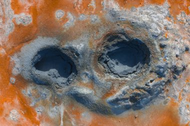 İzlanda 'daki iki jeotermal çamur tenceresinin hava görüntüsünü kapatın. Kırık, küllü bir yüzey üzerindeki canlı turuncu ve gri mineral yataklarıyla çevrili..