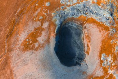 İzlanda 'da turuncu ve gri tonlu, koyu oval çamur tenceresi, mineral yatakları ve buharlı toprak içeren bir jeotermal bölgenin hava görüntüsü..