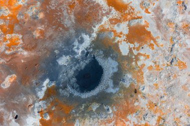 İzlanda 'da turuncu, beyaz ve gri mineral yataklarıyla çevrili bir kraterin yer aldığı bir jeotermal alanın hava görüntüsü..