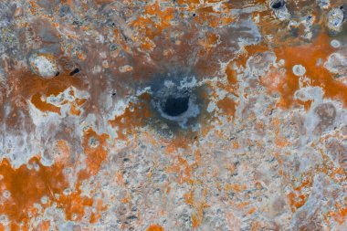 İzlanda 'da canlı turuncu, beyaz ve gri arazi, koyu çamur tenceresi, mineral yatakları ve görünür buhar içeren jeotermal bir bölgenin hava görüntüsü..