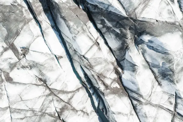 Karanlık volkanik kül çizgileri, karmaşık yarıklar ve engebeli dokuları olan beyaz buzdan oluşan İzlanda buzulunun hava görüntüsünü kapatın..