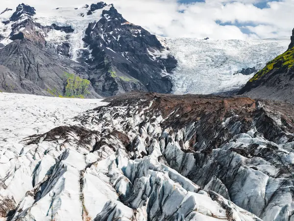Karanlık volkanik kül çizgileri, pürüzlü buz oluşumları ve İzlanda 'da parçalı bulutlu bir gökyüzünün altında yosun kaplı dağları olan buzullar..