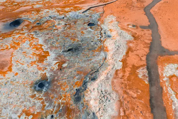 İzlanda 'da turuncu ve beyaz mineral yatakları, koyu çamur kapları, buharlı bacalar ve dolambaçlı karanlık bir yolun yer aldığı jeotermal bir bölgenin havadan görünüşü..