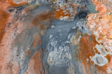 İzlanda 'da canlı turuncu, kırmızı ve gri renkler, buharlı bacalar, kaynayan çamur kapları ve mineral yataklarının yer aldığı jeotermal bir bölgenin havadan görünüşü.