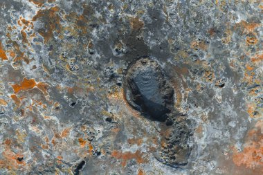 İzlanda 'da gri, turuncu ve pas renginde çatlak araziyle çevrili koyu oval şekilli bir çamur tenceresinin hava görüntüsü jeotermal aktiviteler sergiliyor..