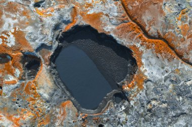 İzlanda 'da koyu renkli bir havuz, canlı turuncu ve pas mineral yatakları, görünür çatlaklar ve desenli toprak desenleri içeren jeotermal bir alan..