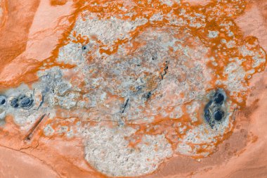 İzlanda 'da turuncu ve beyaz mineral yatakları, kaynayan çamur kapları, buharlı bacalar ve koyu jeotermal havuzların yer aldığı bir jeotermal alanın hava görüntüsü..