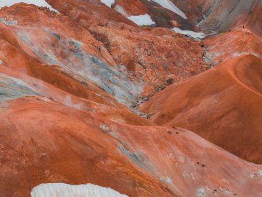 İzlanda 'nın Kerlingarfjoll' unda kar yamaçları ve buharlı bacaları olan canlı turuncu ve kırmızı rhyolite tepeleri, engebeli sırtlarda görünen yürüyüşçülerle.