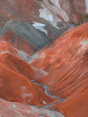 Landmannalaugar, İzlanda 'da canlı kırmızı, turuncu ve yeşil ryolite dağları, dolambaçlı patikaları, kar bantları ve jeotermal buhar bacaları var..