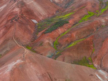 İzlanda 'nın Gökkuşağı Dağları' nın çok renkli ryolit tepeleri, kırmızı, turuncu ve yeşil renklerde, engebeli arazide dolambaçlı bir yol ile.