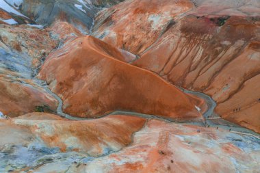 Görüntü Kerlingarfjoll 'un canlı turuncu ve kırmızı rhyolite tepelerini, buhar bacaları, kar bantları ve İzlanda' daki dolambaçlı yollardaki yürüyüşçüleri yakalıyor..