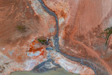 İzlanda 'nın kırmızı, turuncu ve beyaz renkli jeotermal arazisinin hava görüntüsü, kıvrımlı bir dere, görünür çamur kapları ve sağ üst kısımda izler..