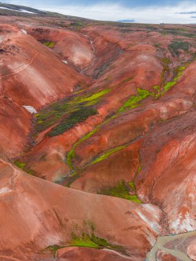 Yeşil yosunlu İzlanda Gökkuşağı Dağları 'nın canlı kırmızı, turuncu ve kahverengi tepeleri. Benzersiz oluşumları ve bulutlu gökyüzünün altında küçük bir dere..