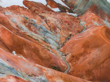 Canlı turuncu, kırmızı ve kahverengi rhyolite dağları beyaz kar yamaçları ve İzlanda 'nın Landmannalaugar kentindeki engebeli araziden geçen bir dere..