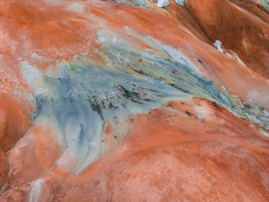 İzlanda 'da kırmızı turuncu arazi, mavi ve yeşil mineral çizgileri ve pürüzsüz, dalgalı yüzeyi olan jeotermal bir bölgenin havadan görünüşü..