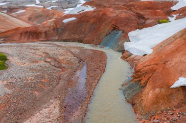 Kırmızı ve turuncu rhyolite tepeleri karla kaplı ve arazide dolanan tortularla İzlanda 'nın dinamik manzarasını gözler önüne seriyor..