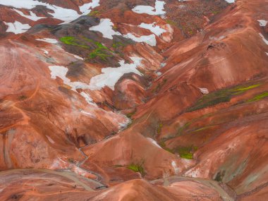 İzlanda 'daki Gökkuşağı Dağları' nın gökkuşağı manzarasında kırmızı, turuncu ve kahverengi rhyolit tepeler, yeşil yosun, beyaz kar ve dolambaçlı yollar yer almaktadır..