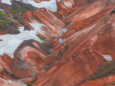 Canlı kırmızı, turuncu ve kahverengi ryolit dağları, beyaz kar yamaları ve İzlanda 'nın dağlık bölgelerindeki jeotermal bacalardan yükselen buhar..