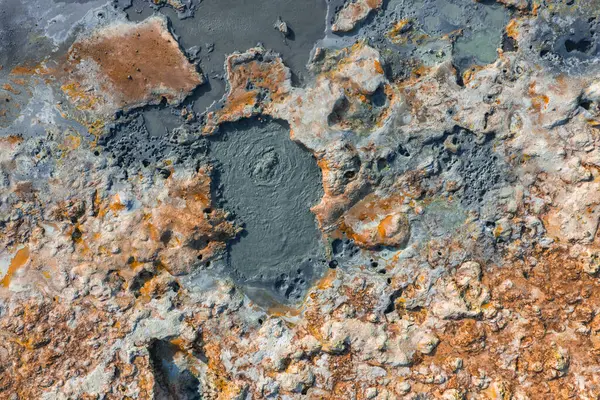 İzlanda 'da kaynayan çamur kapları, canlı turuncu ve gri mineral yatakları ve engebeli desenli arazisi olan jeotermal bir bölgenin hava görüntüsü..