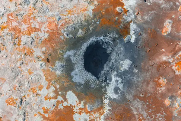 İzlanda 'da, turuncu, kahverengi ve beyaz mineral yataklarıyla çevrili kaynayan bir jeotermal çamur tenceresinin hava görüntüsü benzersiz jeolojik dokular sergiliyor..