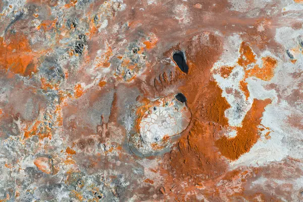 İzlanda 'da canlı turuncu, kırmızı ve beyaz renkleri olan jeotermal bölgede çatlak, soluk yüzeylerle çevrili iki koyu oval havuz bulunuyor..