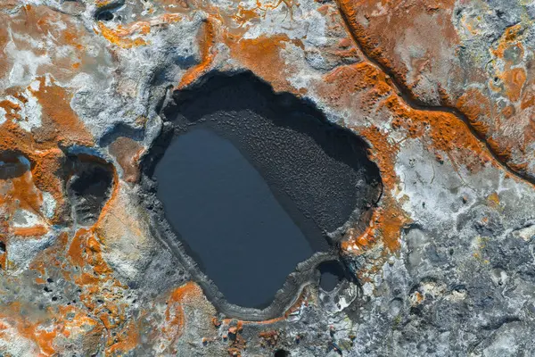 İzlanda 'da koyu renkli bir havuz, canlı turuncu ve pas mineral yatakları, görünür çatlaklar ve desenli toprak desenleri içeren jeotermal bir alan..