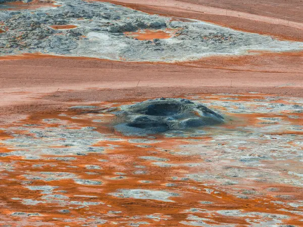 İzlanda 'daki düz arazide merkezi bir çamur tenceresinin etrafında turuncu ve beyaz mineral birikintileri, jeotermal aktiviteler ve benzersiz dokular sergileniyor..