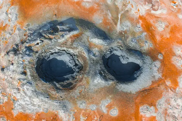Turuncu ve beyaz mineral yataklarıyla çevrili iki kaynayan çamur tenceresinin hava görüntüsü İzlanda 'nın volkanik arazisindeki jeotermal aktiviteyi gösteriyor..
