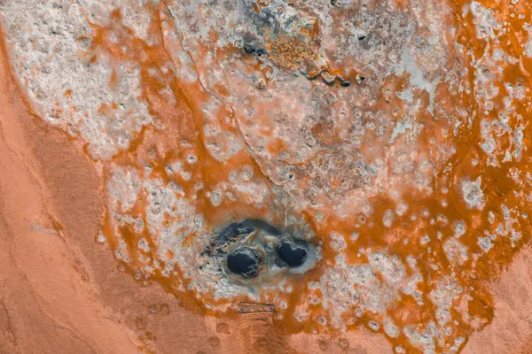 İzlanda 'da turuncu ve beyaz mineral yatakları, desenli yüzeyleri ve merkezinde iki koyu dairesel çamur kapları olan bir jeotermal alanın hava görüntüsü..