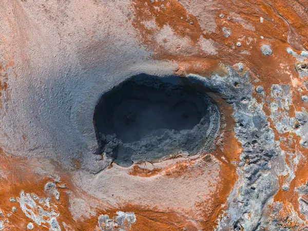 İzlanda 'da, turuncu ve gri mineral yataklarıyla çevrili kaynayan bir jeotermal çamur tenceresinin hava görüntüsü. Arazi canlı jeotermal aktiviteler sergiliyor.