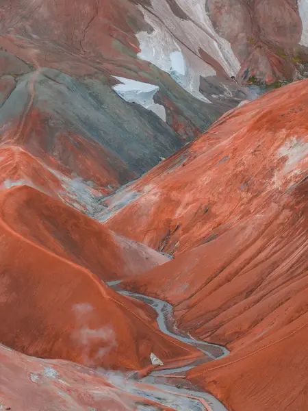 Landmannalaugar, İzlanda 'da canlı kırmızı, turuncu ve yeşil ryolite dağları, dolambaçlı patikaları, kar bantları ve jeotermal buhar bacaları var..