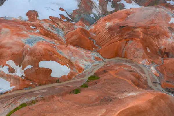Turuncu, kırmızı ve sarı renkli İzlanda Gökkuşağı Dağları 'nın hava manzarası ve engebeli arazide dönen bir dere..