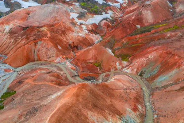 Landmannalaugar, İzlanda 'daki canlı rhyolite dağları, kırmızı, turuncu ve kahverengi renkleri, yeşil yosunları, kar yamaları ve aşağıda dönen bir nehri vardır..
