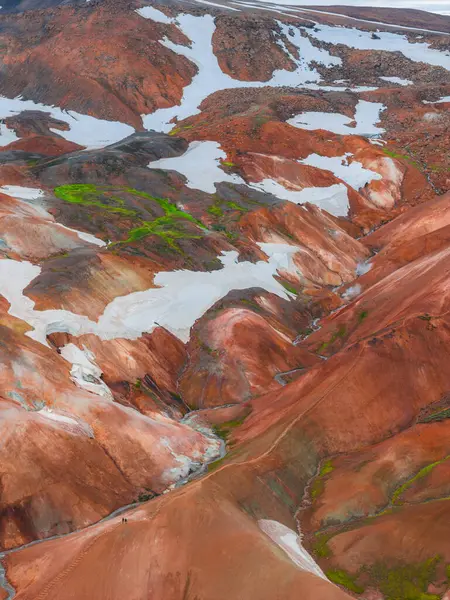 Landmannalaugar, İzlanda 'daki canlı rhyolite dağları, kırmızı, turuncu ve kahverengi renkler, kar yosunları, yeşil yosunlar ve görünür iki küçük figür..