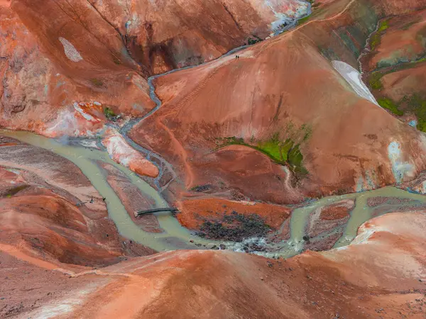 Kerlingarfjoll 'un canlı rhyolite tepeleri, kırmızı, turuncu ve yeşil renkler, jeotermal dereler, ahşap bir köprü ve görünür yürüyüş yolları..