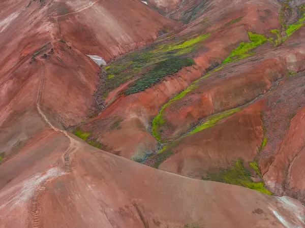 İzlanda 'nın Gökkuşağı Dağları' nın çok renkli ryolit tepeleri, kırmızı, turuncu ve yeşil renklerde, engebeli arazide dolambaçlı bir yol ile.