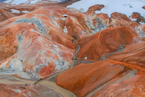 İzlanda 'daki Kerlingarfjoll tepelerinde turuncu, kırmızı ve sarı renkler, buhar bacaları, kar bantları, ahşap bir köprü ve yollar var..