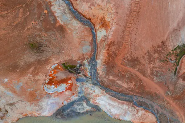 İzlanda 'nın kırmızı, turuncu ve beyaz renkli jeotermal arazisinin hava görüntüsü, kıvrımlı bir dere, görünür çamur kapları ve sağ üst kısımda izler..