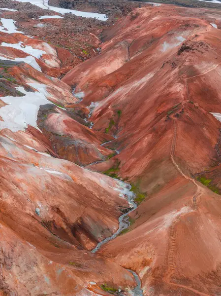 Landmannalaugar, İzlanda 'daki canlı rhyolite dağları, kırmızı, turuncu ve kahverengi renkler, kar bantları, yeşil bitki örtüsü ve dolambaçlı bir akarsu..