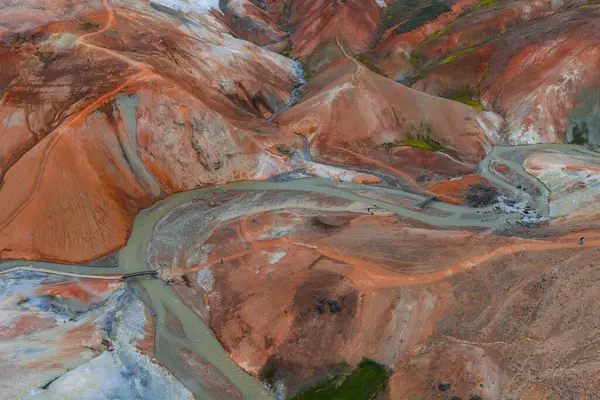 İzlanda 'nın Gökkuşağı Dağları' nın canlı kırmızı, turuncu ve kahverengi renkleriyle hava manzarası. Sarmal bir nehir ve ahşap köprüler engebeli araziyi geçiyor..