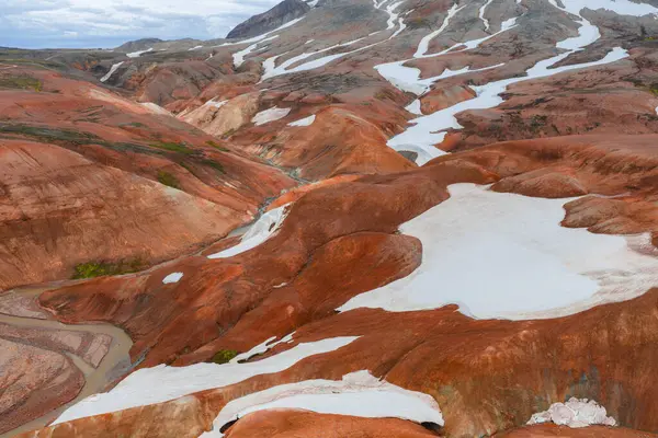 İzlanda 'nın Gökkuşağı Dağları' nın canlı kırmızı, turuncu ve kahverengi rhyolite tepeleri. Beyaz kar yamaları ve araziyi kesen dolambaçlı bir dere..