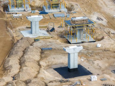 Riga 'dan Jelgava yoluna kadar olan beton köprü iskeleleri kumlu arazide çeşitli aşamalarda, iskeleler, ağır ekipmanlar ve inşaat malzemeleriyle çevrili..