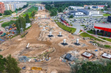 Riga 'dan Jelgava yoluna beton köprü sütunları, ağır makineler, işçiler ve malzemeler ile büyük ölçekli yol inşaatı. Bölgenin çevresindeki kentsel ve ormansal alanlar.